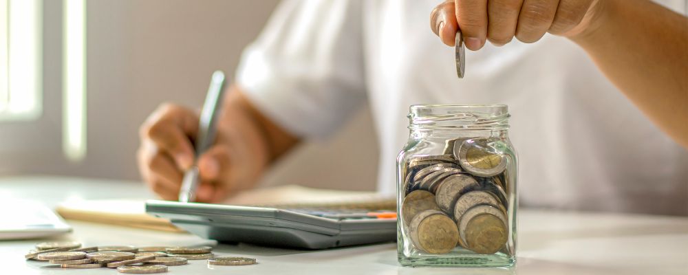 A person putting coins in a jar representing setup cost calculations and ongoing expenses.